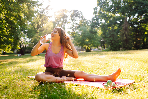 Fitness woman doing yoga, sports exercises in the park. Athletic woman sitting on a mat outdoors on a sunny lawn. Fitness. Active lifestyle.