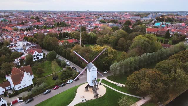 Aerial view of a windmill with cars driving by inBruges, Belgium, City, Canals, Medieval, Architecture, UNESCO World Heritage Site, Historic, Tourism, Culture. Timelapse, orbit wide shot