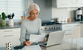 Mature woman, bills and documents on laptop for home mortgage, budget planning and pension research. Freelancer or person on computer, reading paperwork or taxes, asset management and life insurance