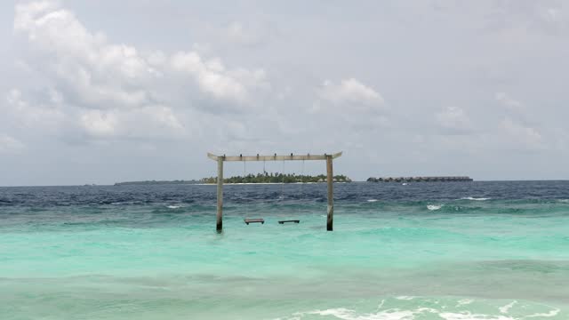 Beach swing and watching ocean waves. Carefree summer moment at ocean beach. Maldives, Indian ocean.