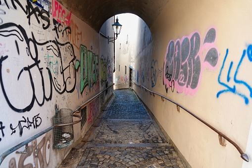 Augsburg, Germany – July 02, 2022: An old arched alley with graffiti, a garbage can and a lantern on the wall in Augsburg, Germany.