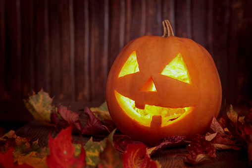 Jack o lanterns  Halloween pumpkin face on wooden background and autumn leafs