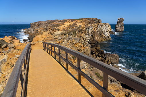 Wooden path in the Papoa island in the site of geological interest of the cliffs of the Peniche peninsula, portugal, in a sunny day with the rock formations.