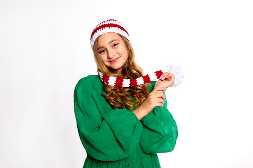happy girl in christmas green dress and red striped knitted hat looking at camera on white background