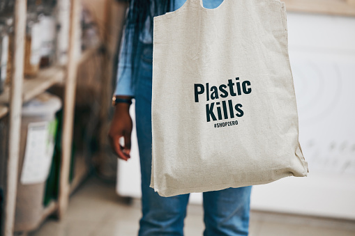 Person in eco friendly grocery store, recycling shopping bag and commitment to climate change at sustainable small business. Zero waste, plastic kills logo and supermarket carbon footprint choice.