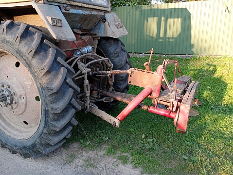 Tractor-mounted mower. The back of a tractor with a red disc mower attached.