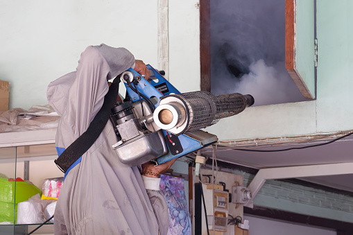 Outdoors Healthcare worker in protective clothing is spraying chemical to eliminate mosquitoes into the door of attic room, close up with copy space