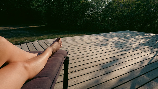 Tanning and sunbathing at sunset. Beautiful woman legs sunbathing on lounger at the terrace.