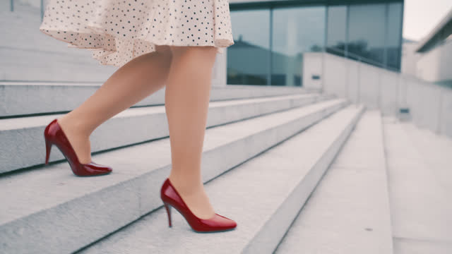 SLO MO An unrecognizable woman in skirt and burgundy stilettos walks down the stairs in front of a modern building