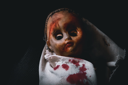 A baby horror doll covered in blood in the dark.