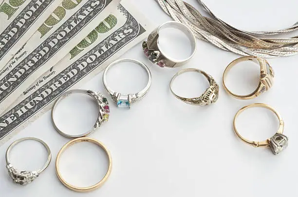 Gold, white gold, and silver jewelry pictured with 100 dollar bills to illustrate, "cash for gold".