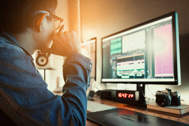 Asian  male movie video editor wearing denim jacket, works with footage or video on his personal computer, in his creative office studio. Asian  male movie video editor wearing denim jacket, works with footage or video on his personal computer, in his creative office studio. editing equipment stock pictures, royalty-free photos & images