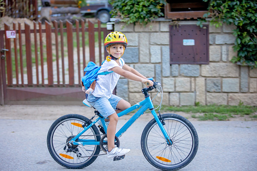 Cute child, boy with helmet and backpack, riding bike at the evening in rural nature, summertime