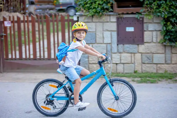 Photo of Cute child, boy with helmet and backpack, riding bike at the evening in rural nature