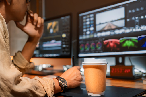 Asian male movie video editor , working with coffee cup , in his creative office studio.