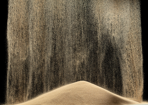 Sand fall down on hill like a rain and splash fly in air. Sand dune hill over wind storm and blast dust splash over mountain. Sunshine rain fall on sand hill wind blow. Black background isolated