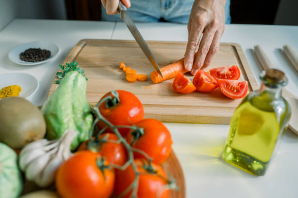 istock High angle of crop anonymous woman slicing fresh carrot on cutting board while preparing salad with tomatoes and parsley in kitchen 1667614940