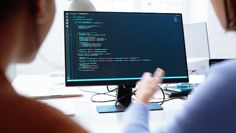 Software developers discussing code on computer screen in coworking office