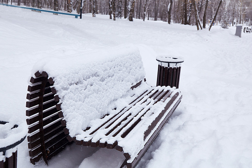A wooden bench covered with snow in the park. Heavy snowfall, snowdrifts. Winter background.