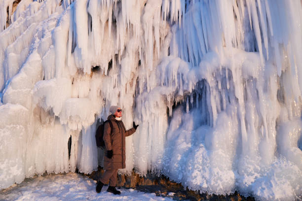 A woman admires huge icicles on the rocks. Winter trip on the frozen lake Baikal.