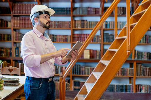 Male architect inspecting the interior of a library using a digital tablet before a renovation
