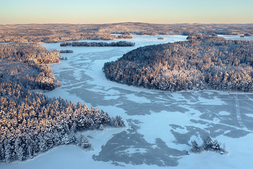Aerial view over a forest and lake (lake; Norra Barken) landscape in winter in the Dalarna region of Sweden.
