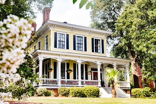 In Macon, USA a two story traditional Southern home with a porch is landscaped with bushes and surrounded by trees in this residential Georgia neighborhood.
