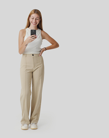 Young smiling woman standing and connecting with her phone, she is social networking and chatting