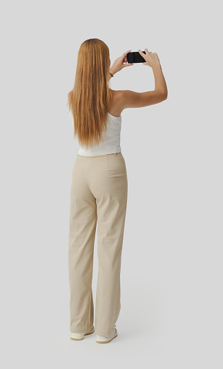 Young beautiful woman taking pictures with her smartphone and sharing online, back view