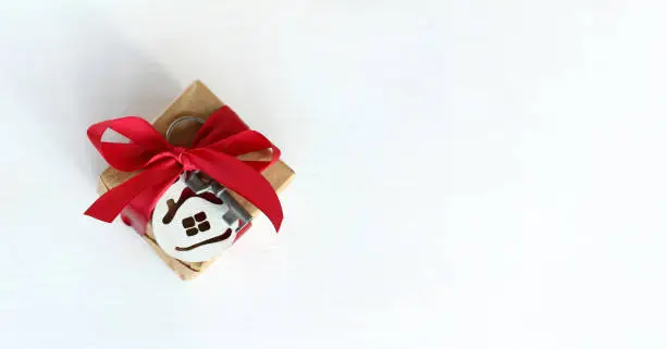 box with a key and a keychain in the shape of a house tied with a red bow on a light background, top view