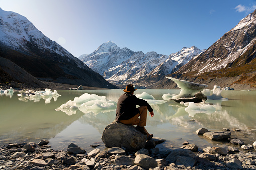 Sporting an Indiana Jones-style hat, a man in his fifties takes in the wonders of beautiful Hooker Lake, whilst the spectacular snow-capped peak of Mt Cook looms majestically in the background.