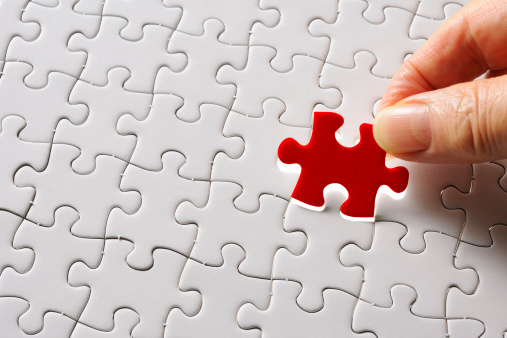 Holding a red final piece of the jigsaw against blank jigsaw puzzle with clipping path.