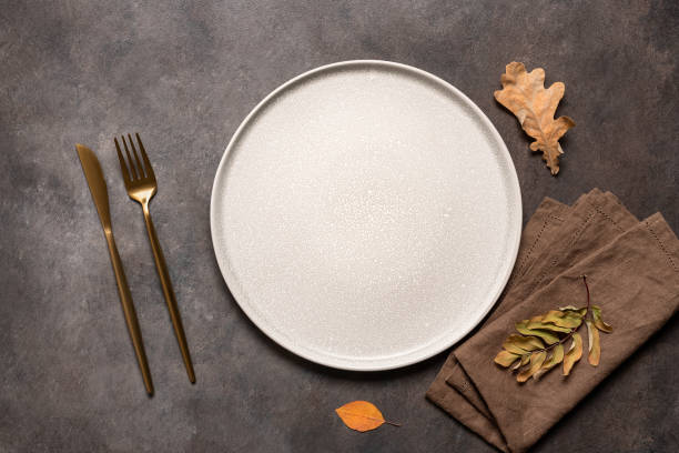 istock Autumn minimal table setting on brown background. Empty beige plate, golden cutlery, linen napkin and dry autumn leaves. Top view, flat lay. 1667819828