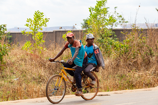Mandoto, Madagascar - November 1st, 2022: Two Malagasy men riding a bike on a countryside road. Two Malagasy men on one bike. One leads the other.