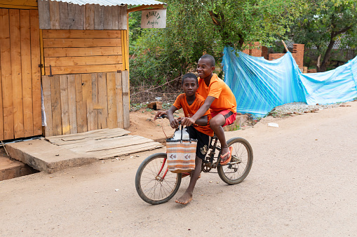 Miandrivazo, Madagascar - November 1st, 2022: Two Malagasy boys riding a bike on a countryside road. One leads the other.