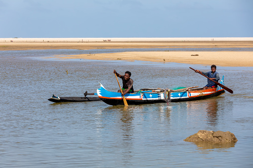 MORONDAVA, MADAGASCAR - NOVEMBER 22, 2022: Fishermen using outrigger canoe carved from tree trunk to fish off the coast of Morondava. The primary source of livelihood in Anakao is fishing.