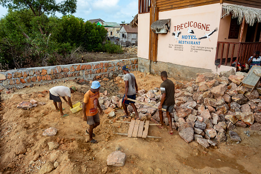 Morondava, Madagascar - November 3rd, 2022: Malagasy men working hard, manually carrying construction stones.