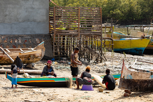 Morondava, Madagascar - November 3, 2022: Fisherman and woman repairing fishing nets at the estuaries of a river, canal Hellot. The woman has a traditionally Malagasy painted face