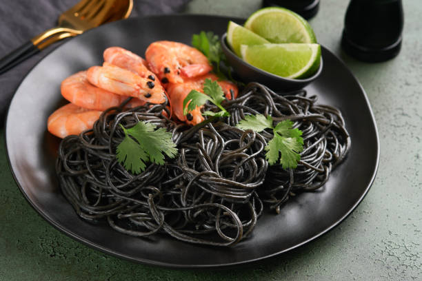 istock Black spaghetti pasta shrimp on black plate on dark concrete table background. Squid ink pasta with prawns. Pasta seafood. Top view on green stone table. Mediterranean traditional cuisine dish. 1667855524