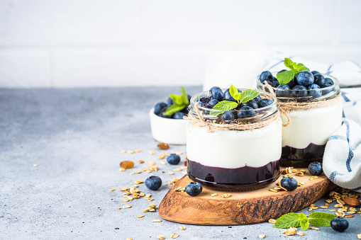 Parfait with blueberry and jam in glass jars at light background. Healthy dessert or snack.
