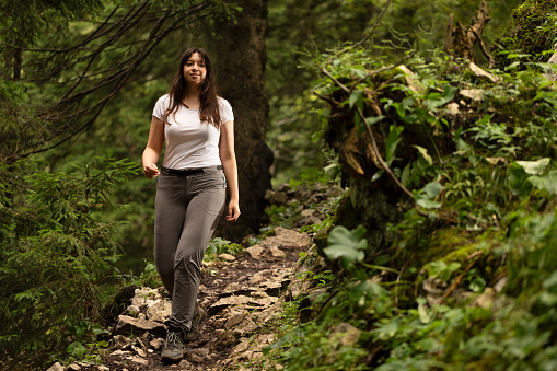 Young adult woman with hiking poles and backpack on the trail post in the woods in the mountains