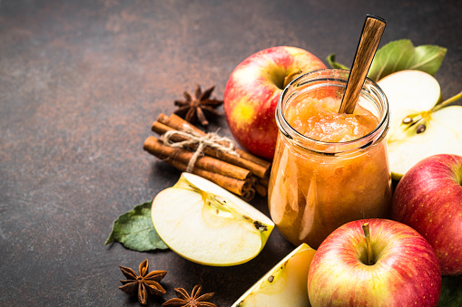 Apple jam in the glass jar and fresh apples and spices on dark background.
