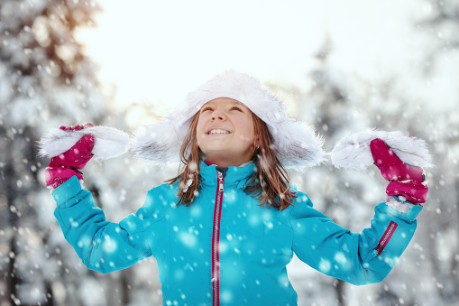 Cute little girl in winter clothes is having fun with raised arms in snowy winter day.