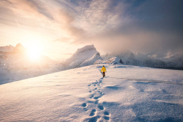 montañero caminando con huella en tormenta de nieve y amanecer sobre montaña nevada en isla senja - winter sunrise mountain snow fotografías e imágenes de stock
