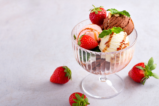 Ice cream scoops in a glass bowl, chocolate, vanilla and strawberry taste on light gray table, top view, copy space