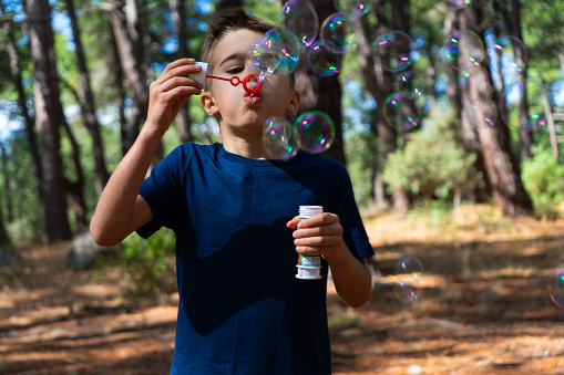 Boy in nature blowing to make lots of soap bubbles
