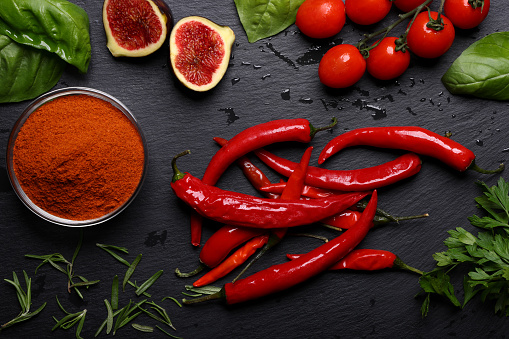 Bowl with aromatic paprika powder and fresh bell peppers on grey wooden table
