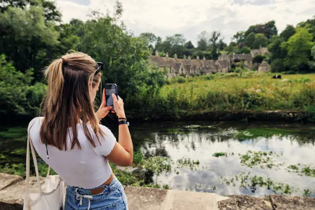 Teenage girl enjoying summer vacations in Cotswolds, Gloucestershire, United Kingdom. 
She is photographing the famous row of houses in Bibury.
Shot with Canon R5
