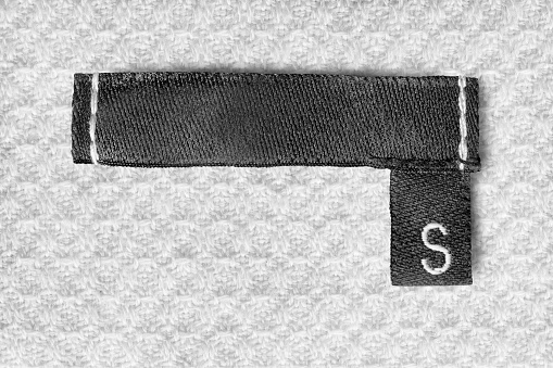 Size S clothes label on white cotton fabric background closeup