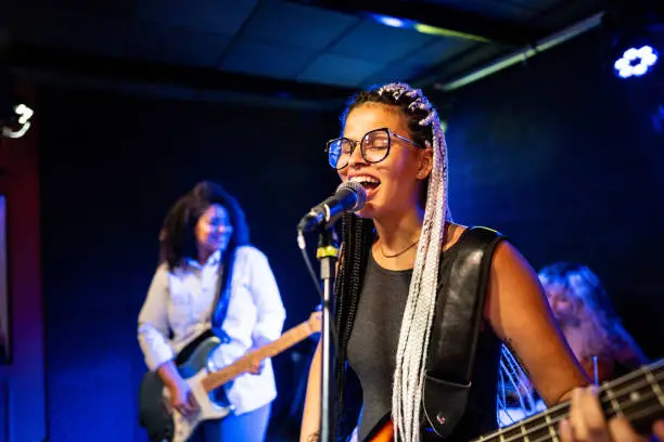 Photo of Young woman singing and playing bass on a show